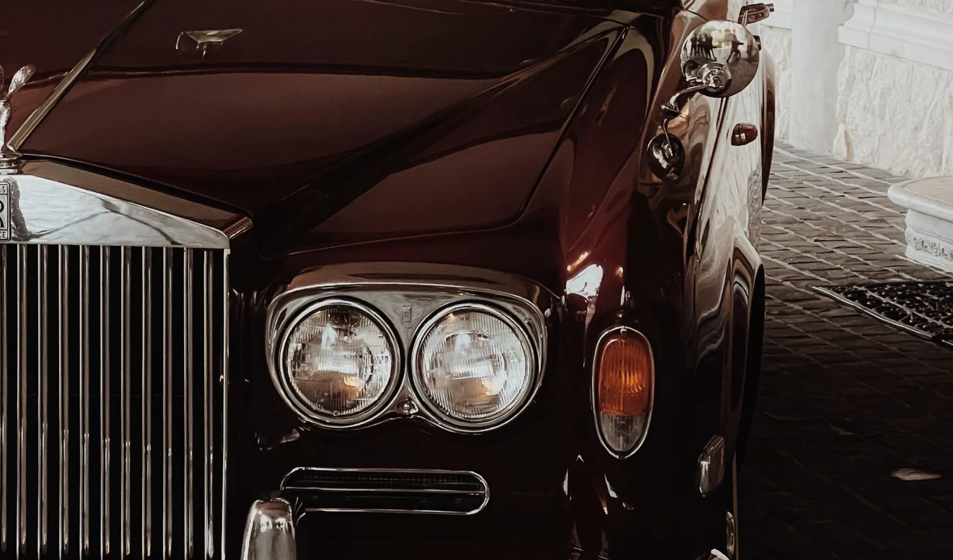 Front grille and headlamps of a classic burgundy Rolls-Royce in a stone courtyard